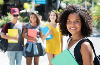 Young woman holding a book with her fellow students standing behind her. 