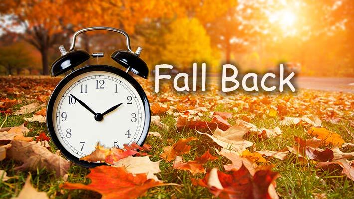 Alarm clock in a field of leaves with the text, Fall Back. 