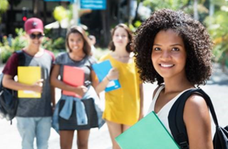 Young woman holding books with her peers standing behind her. 